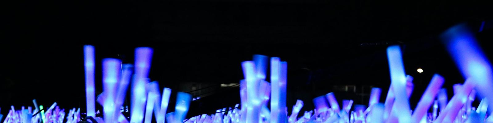 Tłum fanów na koncercie unosi świecące na niebiesko lightsticki w ciemności